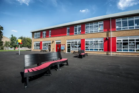 The outdoor play area at John Ray Infant School in Essex, featuring modern aluminium standing seam roofing, red soffit cladding, and a covered entrance. S & G Industrial Roofing Ltd installed high-performance roofing and rainwater drainage systems to ensure durability and weather resistance.
