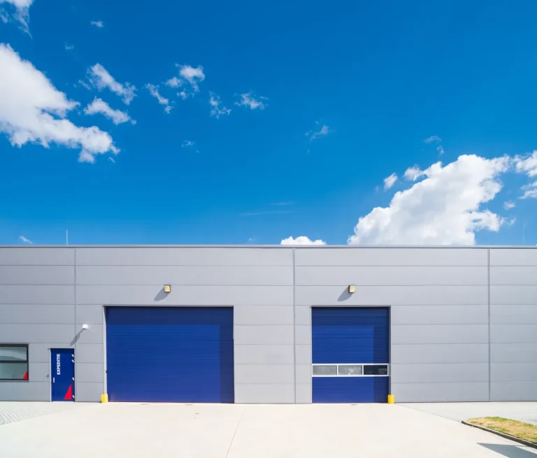 Exterior view of an industrial facility featuring composite wall cladding with integrated insulation, installed by S and G Industrial Roofing. The grey panels contrast sharply with bright blue roller doors, offering enhanced thermal performance and structural integrity.